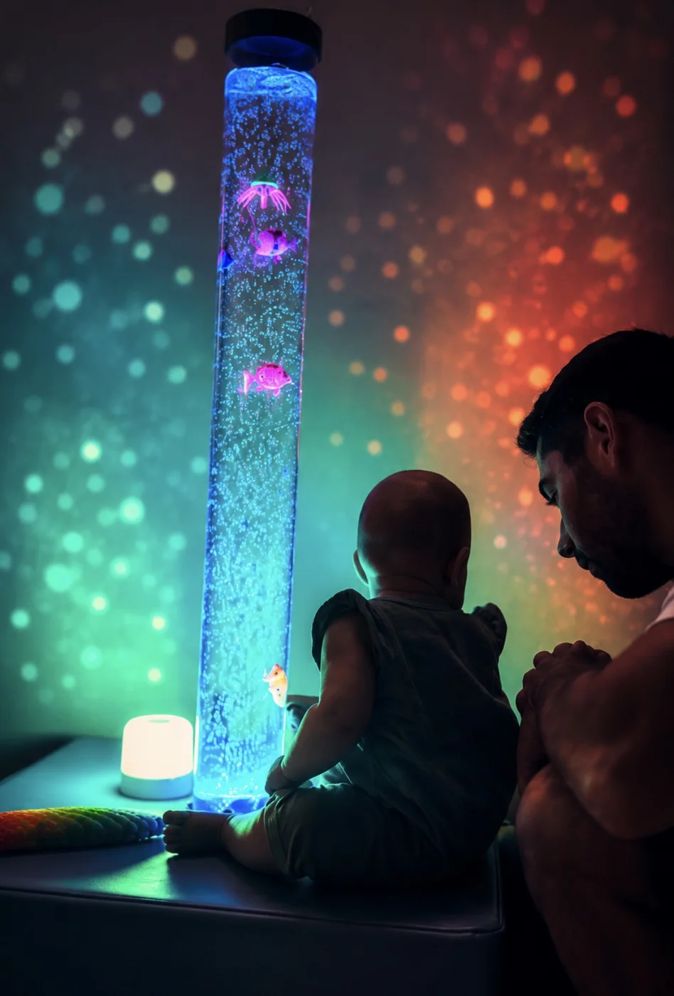 Un bébé et son parent devant le tube à bulles lumineux
